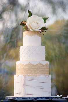 a three tiered white wedding cake with gold trimmings and a flower on top