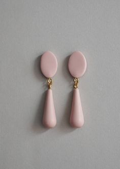 two pink drop earrings with gold accents on a gray background, one is shaped like a tear and the other is shaped like a circle