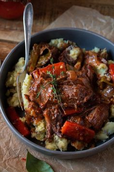 a bowl filled with meat and vegetables on top of a wooden table next to a spoon