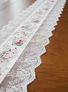 white lace with pink flowers on it sitting on a wooden floor next to a wall