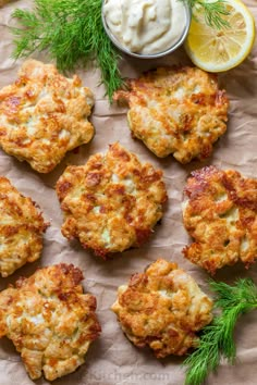 crab cakes with lemon wedges and dill on parchment paper next to dip sauce