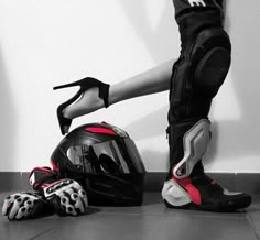 a person standing next to a motorcycle helmet and gloves on the floor in front of a wall