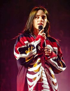 a woman holding a microphone in her right hand and wearing a colorful coat on stage