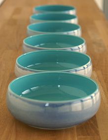 four bowls are lined up on a wooden counter top, one is blue and the other has white rims