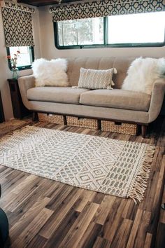 a living room area with couch, rug and window in the back ground next to wood flooring