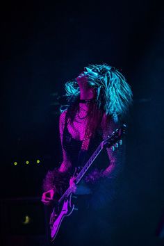 a woman with long hair playing a guitar on stage at a music festival in the dark