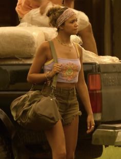 a woman in short shorts and a tank top walking past a truck with bags on the back