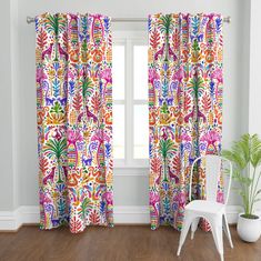 a white chair sitting next to a window covered in colorful curtain panels and drapes