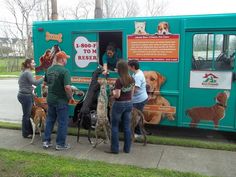 several people standing in front of a food truck with dogs on leashes and one person holding the door open