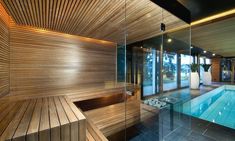 an indoor swimming pool surrounded by glass walls and wooden steps leading to the upper level