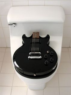 a black electric guitar sitting on top of a toilet seat in a bathroom stall with white tile flooring