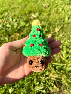 a small teddy bear with a green christmas tree on its head is held in someone's hand