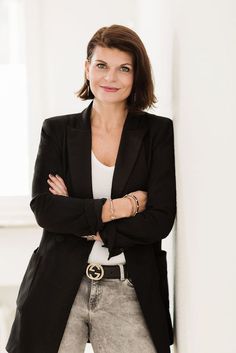 a woman standing in front of a white wall with her arms crossed and looking at the camera