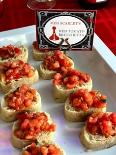 small pieces of bread topped with tomatoes on top of a white plate next to a red table cloth