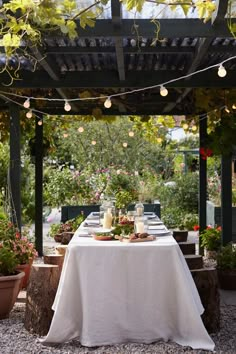 the table is set up for an outdoor party with lights strung from the pergolated roof