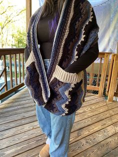 a woman standing on a porch wearing a crocheted shawl and jeans with her hands in her pockets