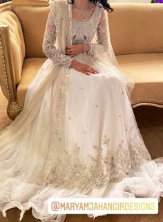 a woman is sitting on a couch wearing a white wedding dress with long sleeves and beadings