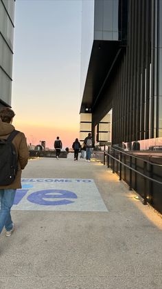 people are walking down the sidewalk in front of an office building at sunset or dawn