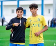 two young men standing next to each other on top of a soccer field with one pointing at the camera