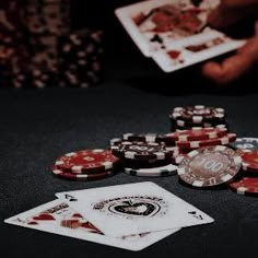 playing cards and poker chips on a black table with someone holding up their hand in the background