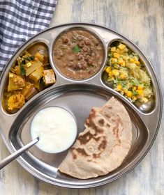 a metal plate topped with different types of food next to a cup of milk and spoon