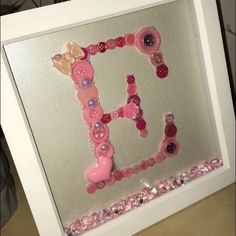 the letter f is made out of buttons and other things on display in a white frame