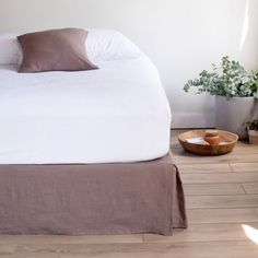 a bed sitting on top of a hard wood floor next to a potted plant