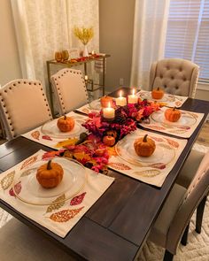 a dining room table set for thanksgiving dinner with candles and pumpkins on the plates