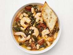 a white bowl filled with shrimp and spinach soup next to a piece of bread