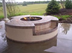 a fire pit sitting on top of a patio next to a lush green field with trees