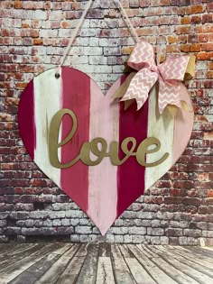 a heart shaped sign with the word love hanging on a brick wall next to a wooden floor