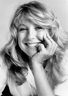 a black and white photo of a woman with her hand on her chin smiling at the camera