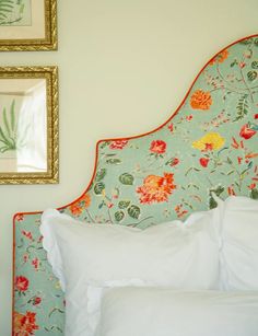 a floral headboard with white sheets and pillows in a hotel room next to two framed pictures