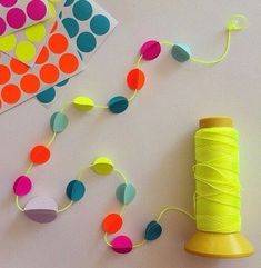 a spool of yellow thread next to a spool of neon colored paper on a white table