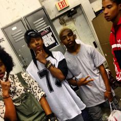 four young people standing in front of lockers talking on their cell phones while one man holds his hand up to his mouth