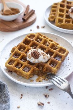 two plates with waffles and whipped cream on them, one has a fork