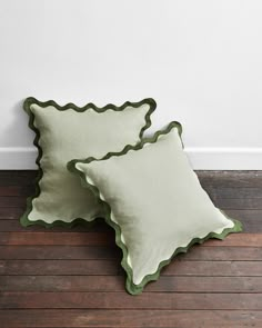 two green scalloped pillows sitting on top of a wooden floor next to a white wall