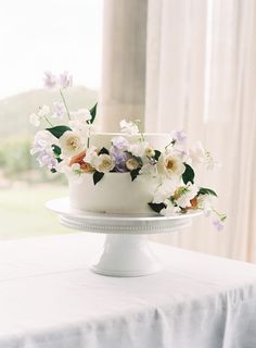 there is a white cake with flowers on the top and bottom, sitting on a table in front of a window