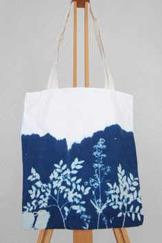 a blue and white tote bag sitting on top of a wooden easel next to an easel