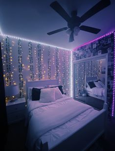 a white bed sitting under a ceiling fan in a room with lights on the walls