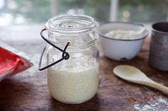 a glass jar filled with food sitting on top of a wooden table next to bowls and spoons