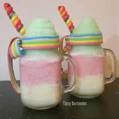 two mugs filled with ice cream and rainbow colored toppings on top of a table