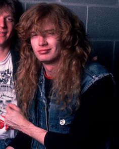 two men with long hair are posing for a photo in front of a brick wall