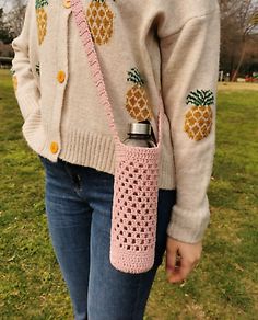 a woman standing in the grass with a pink crocheted purse on her shoulder