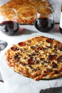 two pizzas and three glasses of red wine on a table with utensils