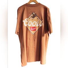 Coors Beer "Rodeo Club" Shirt Featuring A Cowboy With Lasso On Horse On Front And Back. Diamond Design With Logo On Back. Earthy Color Scheme With Espresso, Latte, Cappucino Foam, White, And Red On A Medium Brown Shirt. Official Licensed Coors Product Printed On A Thick Teeluv Shirt. 100% Cotton. Size: Men's L (Women's Xl?) New With Tag. American Golden Mountains Lager Alcohol Usa Co U.S.A. U.S. United States Of America Alcoholic Bar Beverage Golden Colorado Bar Drinking Games Pbr College Pong D Coors Rodeo Shirt, Coors Light Beer Poster, Coors Light Shirt, Vintage Budweiser Shirt, Miller High Life, Lounge Pajamas, Brown Shirt, Coors Light, High Life