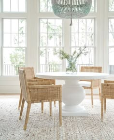 a white table with four chairs around it in front of two windows and a chandelier