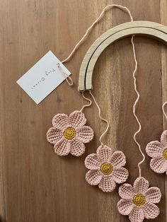 crocheted flowers are hanging from a string on a wooden table next to a piece of wood