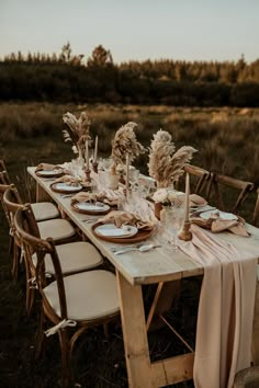 a table set with plates and place settings in the middle of an open field at sunset