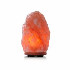 an orange himalayan stone lamp sitting on top of a wooden stand with a white background